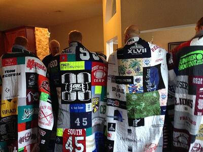 A group of 4 adult brothers wrapped in their T-shirt quilts as seen from the back. by Too Cool T-shirt Quilts