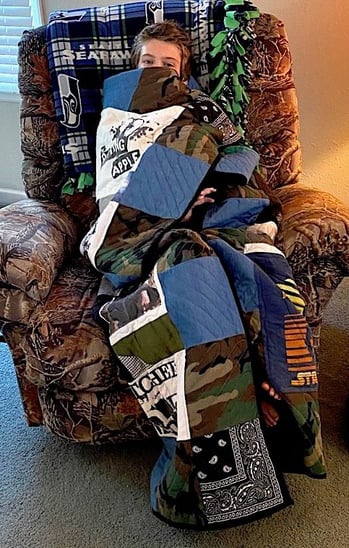 boy wrapped up in a quilt sitting in a chair by Too Cool T-shirt Quilts